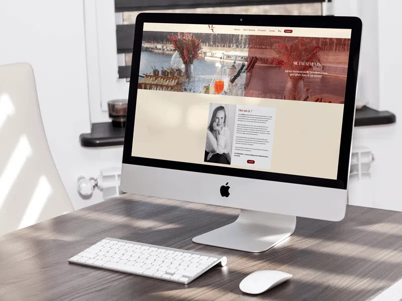 capture-site-mc-evenementspng | Blog Google Ads, Marketing Digital & Business All-in-one iMac on a wooden desk with keyboard and mouse, displaying a website homepage with a river-themed hero image.